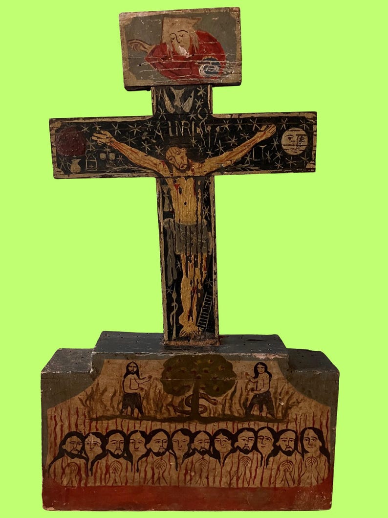 May include: A hand-painted wooden crucifix with a detailed depiction of Jesus Christ on the cross. The cross features painted figures, stars, and the letters INRI. The base shows figures and a tree. The artwork is on a green background.