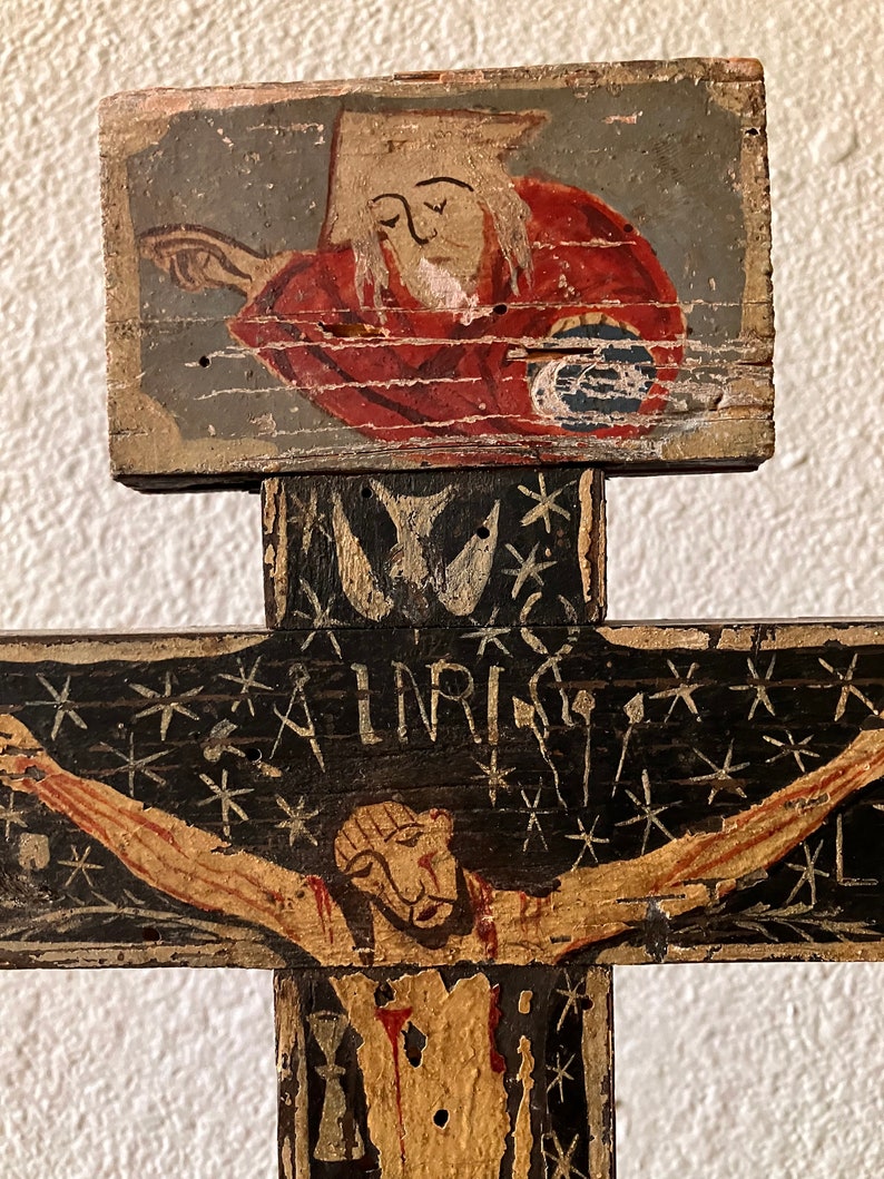 May include: A hand-painted wooden crucifix with a black cross and a figure of Jesus. The cross features the inscription "INRI" and is decorated with stars. The top section depicts a figure in red robes.