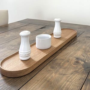 May include: A wooden serving tray with two white ceramic salt and pepper shakers and a white ceramic bowl.