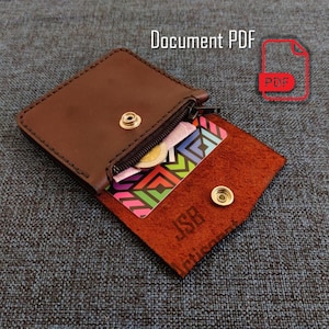 May include: A brown leather wallet with a zipper and snap closure, open to reveal a colorful card and coins. The wallet has the text "JSB Artisan" and the words "Document PDF" are in the top right corner.