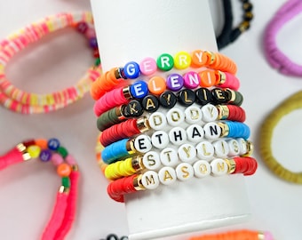 May include: A stack of colorful beaded bracelets with names spelled out in gold letters. The names are "Gerry", "Eleni", "Kylie", "Dody", "Ethan", "Stylist", and "Mason".