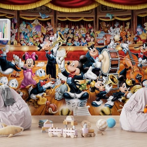 Op de afbeelding: Een muurschildering met een Disney-orkestscène waarin Mickey Mouse dirigeert, omringd door diverse tekenfilmfiguren die instrumenten bespelen op een podium met rode gordijnen, vergezeld door twee lichtgrijze zitzakken en houten speelgoed.