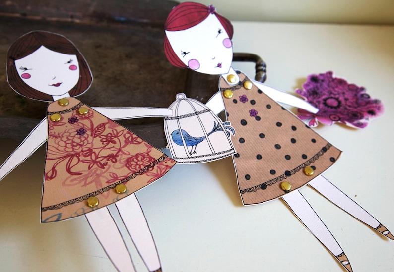 May include: Two paper dolls with brown and black polka dot dresses, one holding a birdcage with a blue bird inside. The dolls have red and brown hair and are wearing gold buttons.