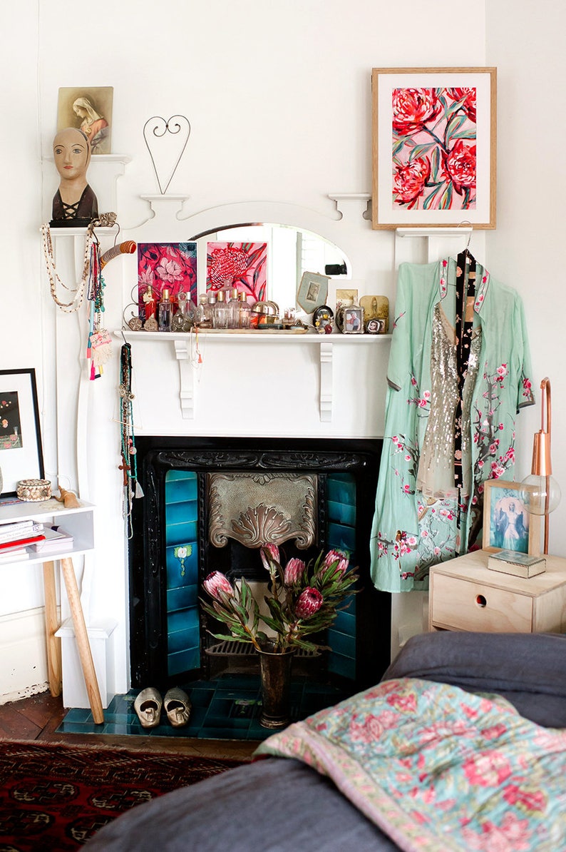 May include: A white fireplace mantel with a black fireplace and blue tiles. The mantel is decorated with a variety of items, including a mirror, candles, and a vase of flowers. A light blue robe with floral embroidery hangs on a hook above the fireplace.