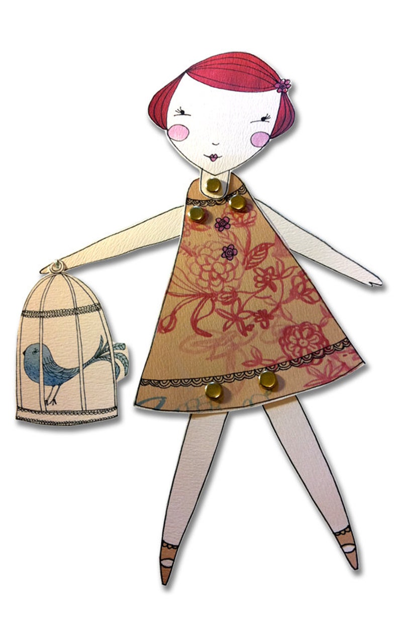 May include: A paper doll with red hair, a floral dress, and a bird in a cage. The doll has a white face with pink cheeks and a red mouth. The dress is brown with pink flowers and a gold trim. The bird is blue with a white belly.