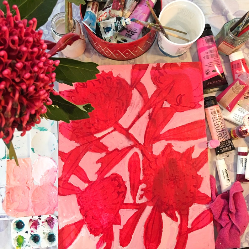 May include: A close-up of a pink canvas with a red floral painting. The painting features large, stylized flowers with red petals and a pink background. The canvas is surrounded by art supplies, including paint tubes, brushes, and a palette.