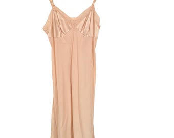 May include: A peach-colored slip dress with adjustable straps and lace trim. The dress is made of a smooth, silky material and hangs from a white hanger. The neckline and hem feature delicate lace detailing.