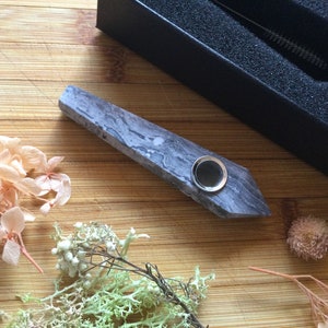 May include: A gray and white marbled stone pipe with a metal bowl. The pipe is on a wooden surface.