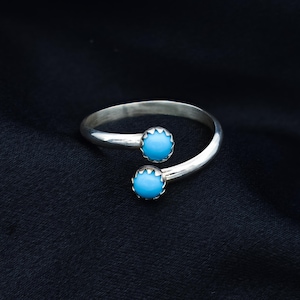 May include: A silver ring with two turquoise stones. The ring is open and can be adjusted to fit different finger sizes.