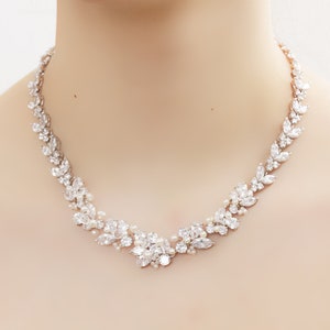 May include: A delicate silver necklace with a floral design featuring clear and white rhinestones. The necklace is on a white background.