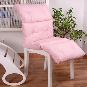 May include: A white chair with a pink padded cushion. The cushion has a tufted design and is attached to the chair with straps.