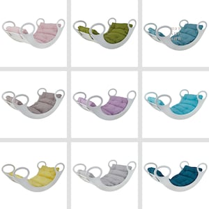 Op de afbeelding: Negen witte houten schommels met verschillende gekleurde kussens. De kussens zijn roze, groen, blauw, grijs, paars, lichtblauw, geel, grijs en teal.