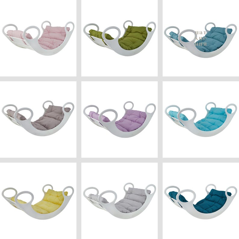 Op de afbeelding: Negen witte houten schommels met verschillende gekleurde kussens. De kussens zijn roze, groen, blauw, grijs, paars, lichtblauw, geel, grijs en teal.