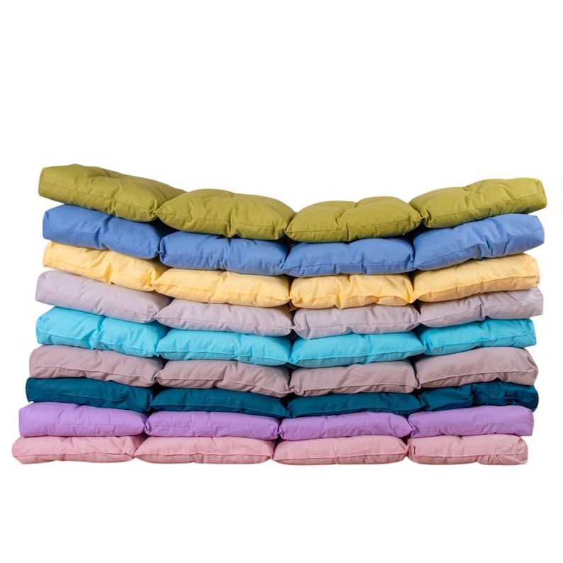 May include: A stack of 12 colorful cushions in various shades of green, blue, yellow, pink, and purple. The cushions are arranged in a staggered pattern, with the top cushion being green and the bottom cushion being pink.