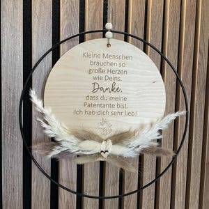 Könnte beinhalten: Ein Holz-Kreis mit einem schwarzen Metallring, der an einer Holzlattenwand hängt. Der Kreis trägt eine Botschaft, die lautet "Kleine Menschen brauchen so große Herzen wie Deins. Danke, dass du meine Patentante bist. Ich hab dich sehr lieb!"
