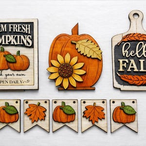 May include: Wooden fall-themed decorations featuring pumpkins, sunflowers, and leaves. Includes a sign that reads "FARM FRESH PUMPKINS" and "pick your own OPEN DAILY". Also includes a sign that reads "hello FALL".