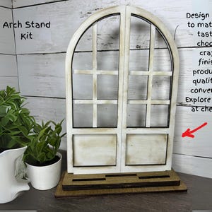 May include: A wooden arch stand kit with a window-like design. The stand is painted white with black trim and has a rectangular base. The text "Arch Stand Kit" is visible. The image also includes a white pitcher, a potted plant, and text.
