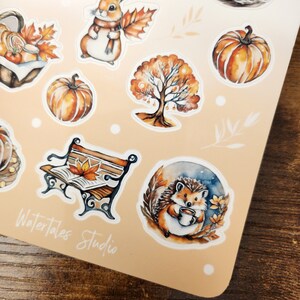 May include: A sheet of fall-themed stickers featuring watercolor illustrations. Designs include pumpkins, a rabbit with a scarf, a tree, a bench with a leaf, and a hedgehog holding a mug. The text "Watertales Studio" is visible.