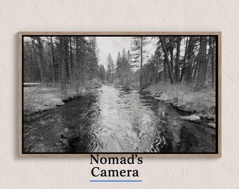 Könnte beinhalten: Schwarz-weiß gerahmte Fotografie eines Flusses, der durch einen Wald fließt. Das Bild zeigt hohe Bäume auf beiden Seiten des Flusses, mit dem Text "Nomad's Camera" am unteren Rand.