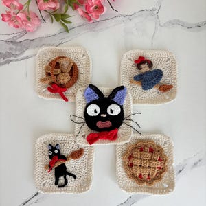 Puede incluir: Cinco cuadrados de ganchillo color crema con personajes y elementos de una película de animación popular. Los diseños incluyen un gato negro con pajarita roja, una niña en una escoba y una tarta. Los cuadrados presentan diseños detallados y coloridos.