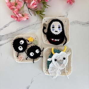 Könnte beinhalten: Drei handgefertigte Häkelquadrate mit Figuren aus dem Zeichentrickfilm Spirited Away. Die Quadrate zeigen eine schwarze Kreatur, eine Figur mit weißer Maske und eine weiße yakartige Kreatur mit gelben Hörnern. Die Quadrate sind beige mit weißem Rand.