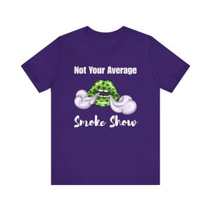 May include: A purple t-shirt featuring a graphic of green lips with cannabis leaves and white smoke. The text "Not Your Average Smoke Show" is above and below the graphic in white.