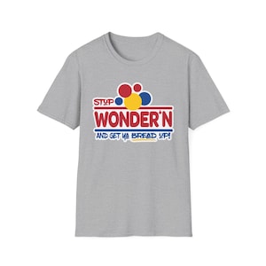 May include: A grey t-shirt featuring the slogan "STOP WONDER'N AND GET YA BREAD UP!" in red, blue, and yellow. The design includes colourful circles above the text.