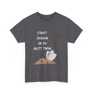 May include: Dark gray t-shirt with the text "START DIGGIN IN YO BUTT TWIN" in white. A cartoon shovel is digging into a pile of dirt. The shirt is a casual wear item.