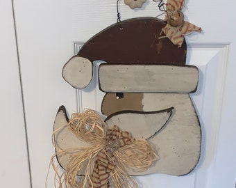 May include: A wooden Santa Claus head with a brown hat, white beard, and a straw bow. The Santa head is attached to a long, brown and white striped ribbon.