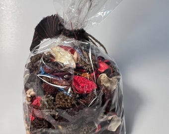 May include: A clear cellophane bag filled with a mix of dried potpourri. The potpourri includes red, brown, and cream-colored dried flowers and botanicals. The bag is tied with a dark brown ribbon and twine.