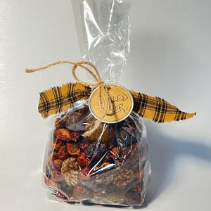 May include: A clear cellophane bag filled with dried fruit and spices, tied with twine and a yellow and black plaid ribbon. A small, round tag with the words "MULLED BER" is attached to the twine.