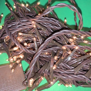 May include: Brown string fairy lights with warm white LED bulbs. The lights are coiled together and have a small brown box with a power cord.
