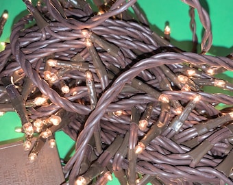 May include: Brown string fairy lights with warm white LED bulbs. The lights are coiled together and have a small brown box with a power cord.