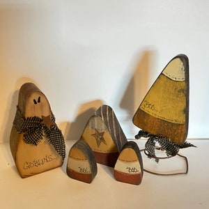 May include: Four wooden Halloween decorations, including a ghost with a black and white checkered ribbon and the words "Goblins" written on it, and three candy corn shaped decorations with the word "Boo" written on them.