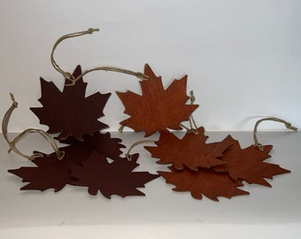 May include: A set of eight brown maple leaf ornaments with twine string for hanging. The leaves are made of wood and have a rustic, natural look.
