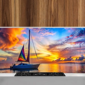 May include: A sailboat with a rainbow sail is anchored in the ocean at sunset. The sky is a vibrant mix of orange, pink, and blue with fluffy clouds.