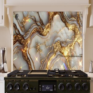 Könnte beinhalten: Eine Küchenrückwand mit einem weißen und goldenen Marmormuster. Die Rückwand befindet sich hinter einem schwarzen Herd mit einem digitalen Display, das "350°" anzeigt.