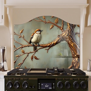 Puede incluir: Un protector de salpicaduras de cocina decorativo con un árbol dorado y marrón y un pequeño pájaro posado en una rama. El protector de salpicaduras está detrás de una estufa de gas negra con una pantalla digital que muestra "350°".