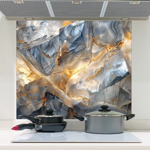 May include: A kitchen backsplash with a modern abstract design featuring a blue and gold marble pattern. Two pots and a pan are on a white stovetop in front of the backsplash.