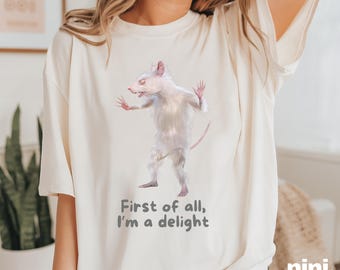May include: A white t-shirt with a graphic of a white rat with the text "First of all, I'm a delight".