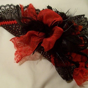 May include: A black and red fabric hat with a large red bow and black feathers. The hat is decorated with black lace and white polka dots.