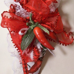 May include: A red and white fabric cone-shaped pincushion with a red ribbon and a red chili pepper. The pincushion is decorated with white lace and red glitter.