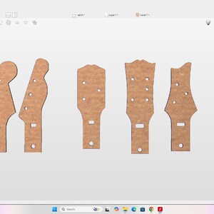 May include: A digital interface displaying five distinct light brown guitar headstock designs arranged horizontally. The software screen includes various toolbars, a preview window, and text indicating dimensions of 26.75 inches by 9.0 inches by 0.25 inches.