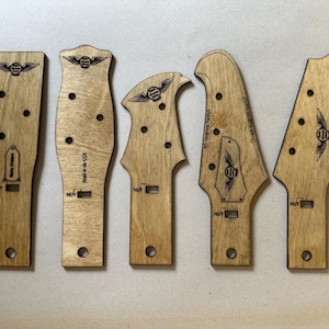 Puede incluir: Cinco plantillas de clavijero de guitarra de madera de varias formas. Cada plantilla es de color marrón claro con un logotipo y texto grabados en oscuro. Tienen agujeros pre-perforados y ranuras para la cejuela. El texto "Made in the USA" es visible en una.