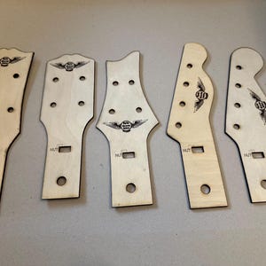 May include: Five unfinished wooden guitar neck blanks with a logo of a winged circle and the word "NUT" printed on each.