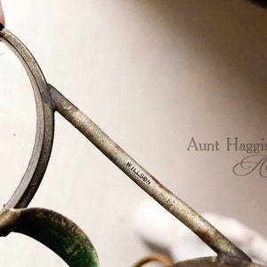 May include: Close-up of antique Willson eyeglasses with a silver-toned metal frame. The glasses have round lenses and a bridge. The text "WILLSON" is visible on the arm. The image is from Aunt Haggis's Attic.
