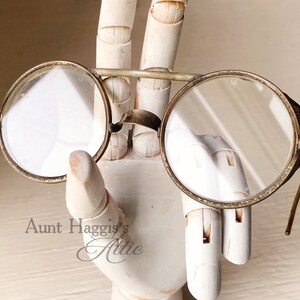 May include: Antique round eyeglasses with a silver-colored frame and clear lenses. The glasses have small side shields and thin, curved temples. The image includes the text "Aunt Haggis's Attic".