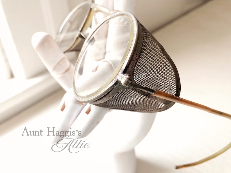 May include: Vintage steampunk-style goggles with clear lenses and a mesh side shield. The goggles have a metal frame and brown temples. The image is set against a white background.