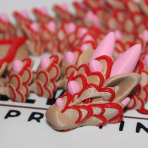 Peut inclure: Une tête de dragon imprimée en 3D avec des détails rouges et roses. La tête de dragon est en plastique brun clair et a une surface texturée.