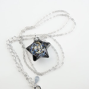May include: A silver chain necklace with a black star-shaped pendant. The pendant has a swirling design of gold and blue glitter.